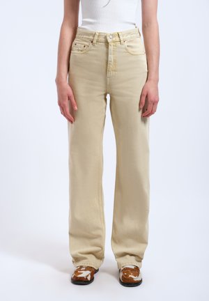 Beige wide-leg jeans made of denim, featuring a high waist, front pockets, and contrasting stitching. Worn with patterned slip-on shoes.