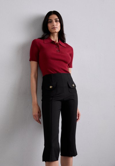 Röd ribbad topp med kort ärm, krage och tre knappar, tillsammans med högmidjade svarta cropped byxor med guld-accenterade fickor.