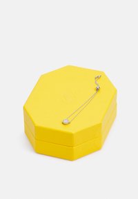 Gelbe sechseckige Schmuckschatulle mit einer strukturierten Oberfläche, die eine silberne Halskette mit einem runden Anhänger und zwei Kettenlängen enthält.