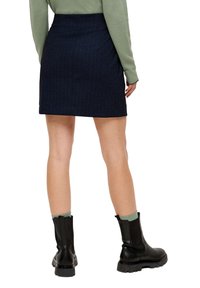 Navyblau gestreifter Minirock aus gewebtem Stoff, mit taillierter Passform und Gesäßtaschen, kombiniert mit schwarzen Stiefeln und grünen Stricksocken.