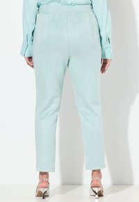 Light turquoise tapered pants made of soft, suede-like material. Features elastic waistband and minimal detailing, paired with silver heels.