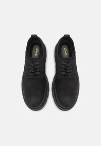 Schwarze Lederschuhe mit glatter Textur, runder Zehenpartie, Schnürdesign und Gummisohlen, mit einem dezenten Clarks-Logo auf der Innensohle.