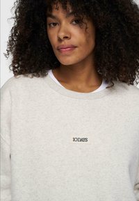 Lichtgrijs sweatshirt van zachte stof, met een ronde hals en een klein zwart "10 DAYS" label op de borst.
