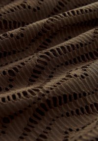 Tissu tricoté marron avec un motif texturé comprenant des trous ouverts et un design nervuré, créant une apparence en couches et ondulée.