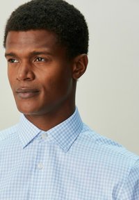 Svetlomodrá károvaná košeľa na gombíky s klasickým golierom. Hladká bavlnená látka a jemná textúra poskytujú elegantný vzhľad.