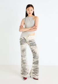 Gray sleeveless top with an asymmetrical hem paired with cream flared pants featuring black abstract patterns, and red heeled shoes.