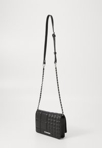 Juodas siuvinėtas per petį nešiojamas krepšys su sidabro grandine ir reguliuojamu odiniu dirželiu, ant priekinių durelių pažymėtas "Steve Madden".