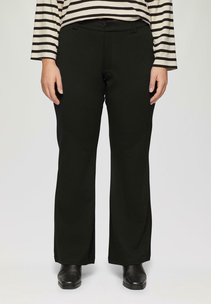 Pantalons larges noirs en tissu doux, avec une taille plate et des poches latérales. Portés avec un haut à rayures à manches longues et des chaussures noires.