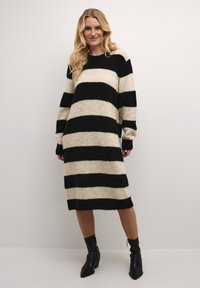 Robe pull rayée en crème et noir, faite d'un tissu doux et texturé. Manches longues et poignets côtelés, longueur genoux.