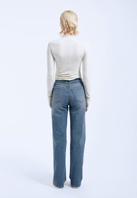 Long-sleeve cream top with gathered back, paired with high-waisted, light blue wide-leg jeans featuring a textured finish and back pockets.