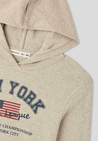 Felpa con cappuccio grigia chiara a coste, con una grafica frontale in blu navy e rosso, contenente testo e una piccola bandiera americana.