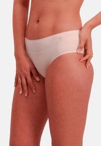 Culotte taille haute beige avec une texture lisse, un design sans coutures et un logo brodé discret sur la ceinture.