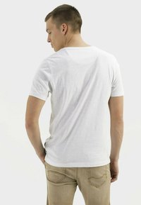 Witte korte mouwen t-shirt met een ronde hals, gemaakt van een textuurstof. Draagt met lichtbeige broek, gezien van achteren.