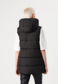 Schwarz gepolsterte Weste mit Kapuze, die horizontale gesteppten Abschnitte und einen lockeren Schnitt aufweist. Hergestellt aus einem weichen Material mit glatter Textur.