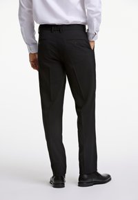 Zwarte, op maat gemaakte broek met achterzakken, gedragen met een lichtgekleurde blouse. Soepele textuur, rechte pijp, gecombineerd met zwarte schoenen.