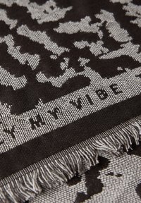 Svart och vit vävd scarf med ett mönster, med texten "MIN VIBB" på en band. Kanterna har en fransig struktur.