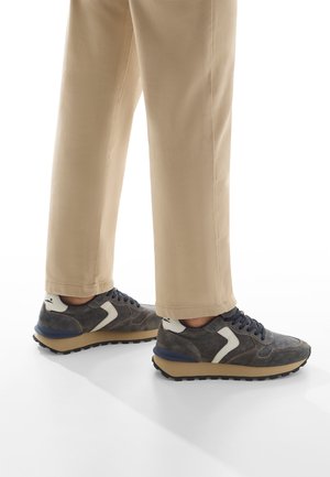 Sneaker grigie con lacci blu navy e dettagli bianchi, caratterizzate da un materiale testurizzato, design a profilo basso e una robusta suola nera.