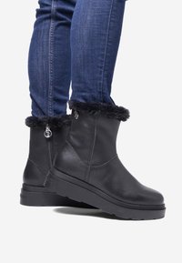 Czarne skórzane botki za kostkę z futrzanym wykończeniem, bocznym zamkiem błyskawicznym i teksturowaną gumową podeszwą, noszone z ciemnoniebieskimi dżinsami.