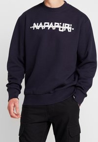 Sudadera azul marino con cuello redondo y puños acanalados. Presenta un logo blanco llamativo en el pecho. Fabricada con un tejido suave y liso.
