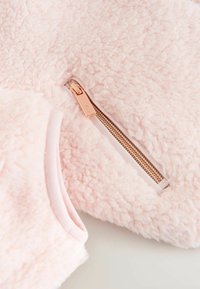 Jasnoróżowa polarowa kurtka z teksturowanym wykończeniem, z detalem w postaci złotego zamka błyskawicznego i miękką, gładką podszewką w mankietach.