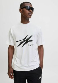 Valge lühikeste varrukatega T-särk, millel on ees suur must graafika ja "CNZ" logo, kantud tumedate pükste ja mustade prillidega.