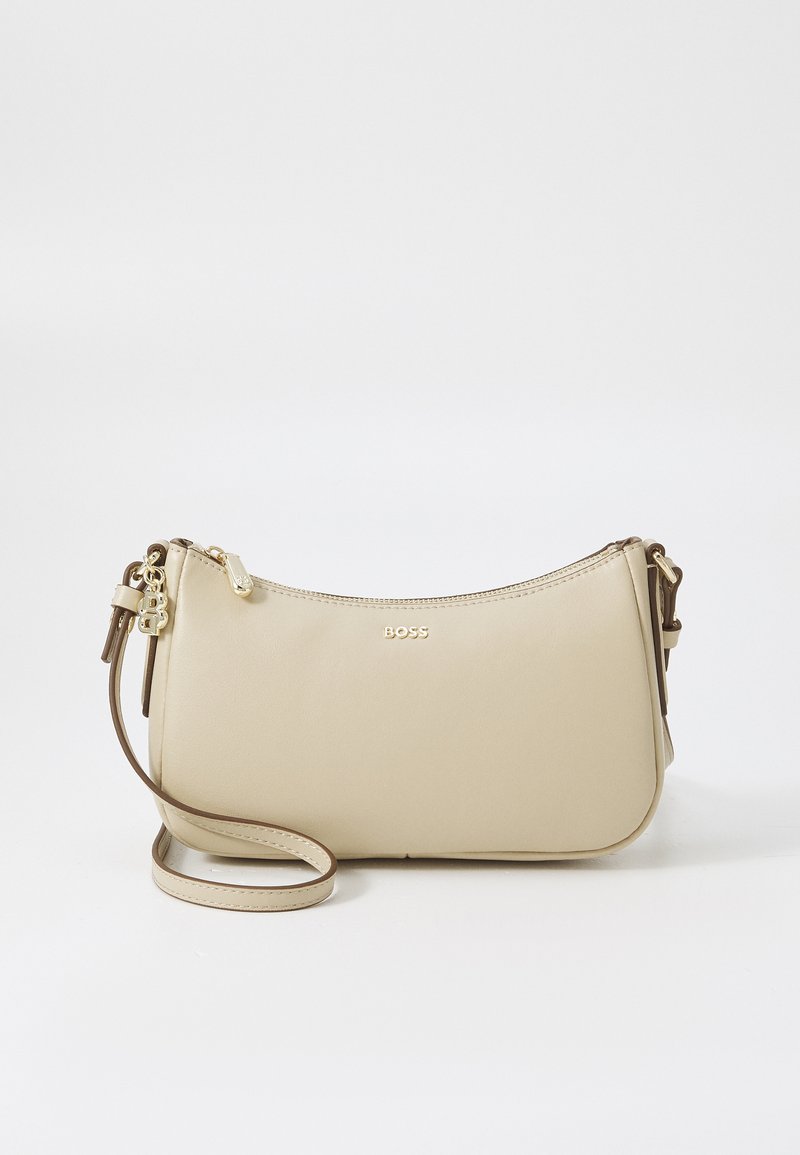 Sac bandoulière en cuir beige avec une forme courbée, des accents en métal doré, une fermeture éclair et une bandoulière ajustable. Logo "BOSS" estampillé à l'avant.