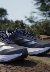 Námorné bežecké topánky s sieťovanými zvrškom, bielymi pruhovanými akcentmi, textúrovanými povrchmi a elegantným dizajnom. Obsahujú gumovú podrážku a polstrovanú pätu.