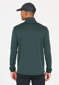 Donkergroen overhemd met lange mouwen en een hoge kraag, met een subtiele horizontale streepstructuur. Draagt een zwart sportbroek, met een aansluitend ontwerp.