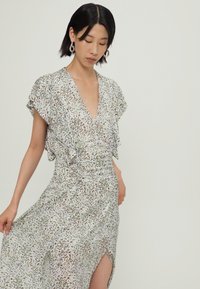 Robe maxi avec un décolleté en V plongeant, des manches courtes à volants et une fente sur le côté. Fabriquée en tissu léger avec un motif abstrait coloré.