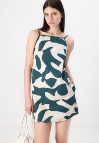Abito senza maniche color crema con un motivo astratto verde. Realizzato in tessuto testurizzato, presenta spalline sottili e tasche laterali.
