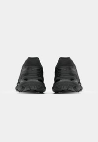 Black athletic shoes with a streamlined design, featuring textured overlays, cushioned soles, and pronounced treads for traction.