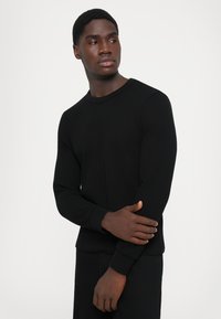 Black long-sleeve sweater made of textured fabric, featuring a round neckline and ribbed cuffs. The fit is casual and relaxed.