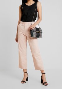 Žena v černém bezramínkovém topu, růžových širokých kalhotách, černých sandálech na podpatku a s černou taškou přes rameno s růžovým vzorem.