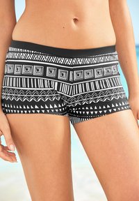 Costumi da bagno a righe bianche e nere con motivi geometrici, una texture liscia e una vita nera a tinta unita.