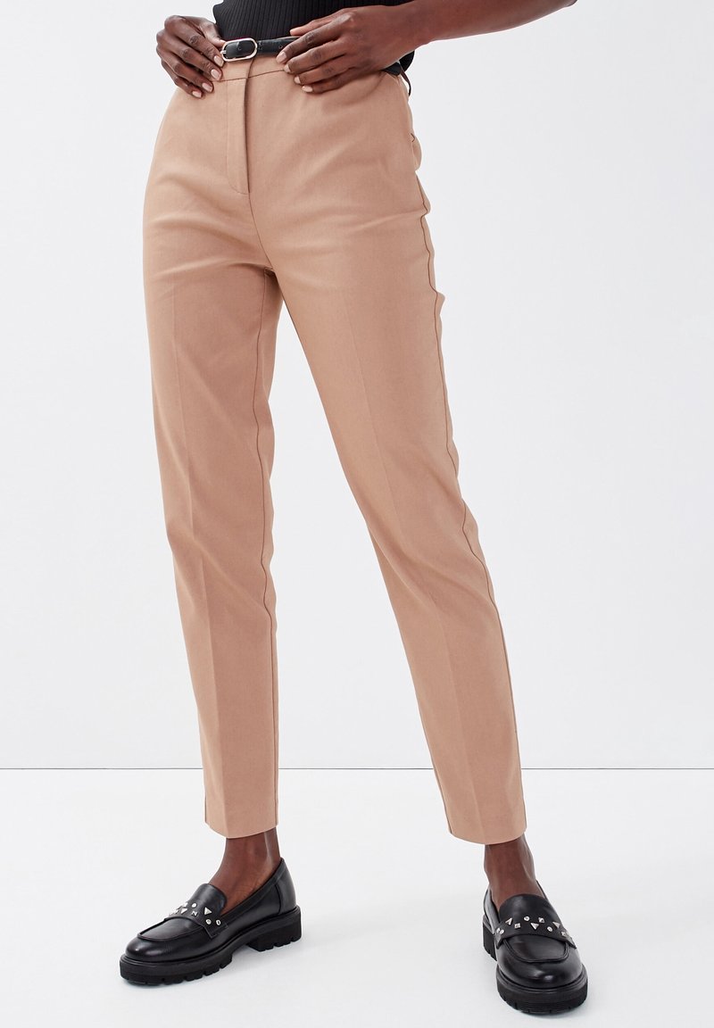 Pantalons beige ajustés avec une coupe slim, accents latéraux et texture lisse. Associés à des mocassins noirs avec des clous en argent.