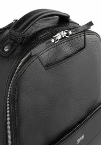 Czarny plecak ze strukturalnej skóry z zamkiem błyskawicznym, wyposażony w górny uchwyt oraz przednią kieszeń z gładkim zamkiem. Widoczne logo marki.