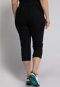 Pantaloni capri neri con vita elasticizzata, texture liscia e aderente, abbinati a scarpe da ginnastica colorate, che mostrano un look informale.