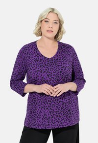Lila Oberteil mit schwarzem Leopardenmuster, V-Ausschnitt und Dreiviertelärmeln, aus weichem Stoff, mit lockerer Passform und ohne sichtbare Hardware.