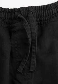 Czarny pas w dresach z elastycznym ściągaczem, ukazujący teksturowany materiał i detale szwów. Zbliżenie na konstrukcję materiału.