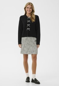 Svart stickad cardigan med pärlknoppsstängningar, i kombination med en svartvit rutmönstrad kjol, svarta loafers och krämfärgade ankelsockor.