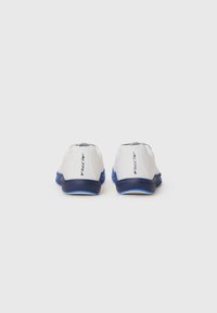 Baskets de course blanches avec une semelle extérieure bleue. Elles présentent une texture lisse, une forme arrondie, et un branding minimal au talon.