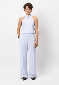 Lichtblauwe haltertop met een keyhole-detail, gecombineerd met bijpassende wijde broek, beide van een gladde stof. Zwarte versierde schoenen.