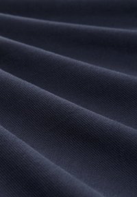 Tissu bleu marine foncé avec une surface texturée, présentant des plis qui créent de la profondeur et de la dimension. Le matériau semble lisse et tissé.