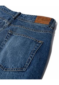 Vaqueros de mezclilla azul oscuro con una etiqueta de cuero estampada con "HEYANNO", detalles de costura visibles y un único bolsillo trasero.
