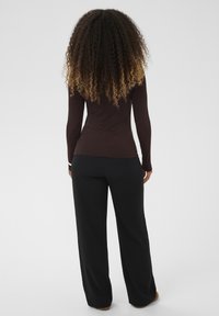 Brun top med lange ærmer og tætsiddende design, kombineret med sorte bukser med vide ben. Tekstureret hår, der går ned til skuldrene.