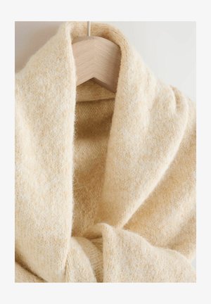 Beiger Strickschal mit einer weichen, strukturierten Oberfläche, der ein breites, fließendes Design aufweist, das elegant fällt. Hängt an einem hellen Holzkleiderbügel.