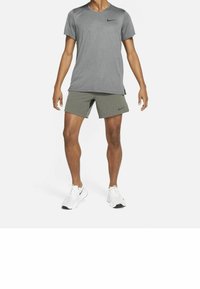 Grå Nike-t-shirt med korta ärmar, kombinerad med olivgröna shorts. Vita sportskor med svarta detaljer. Enkel och funktionell design.