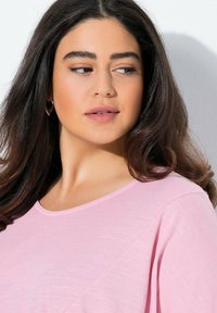 Světle růžový krátký rukáv top s kulatým výstřihem a měkkou texture, charakterizován volnější siluetou a mírně splývavým designem.