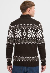Dunkelbrauner Rollkragenpullover mit einem weißen und grauen Schneeflockenmuster auf dem Rücken, gefertigt aus einem strukturierten Strickstoff.