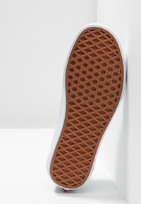 Baskets blanches à semelle en caoutchouc, avec un dessous marron texturé et une bordure supérieure lisse. Le design est simple et sportif.